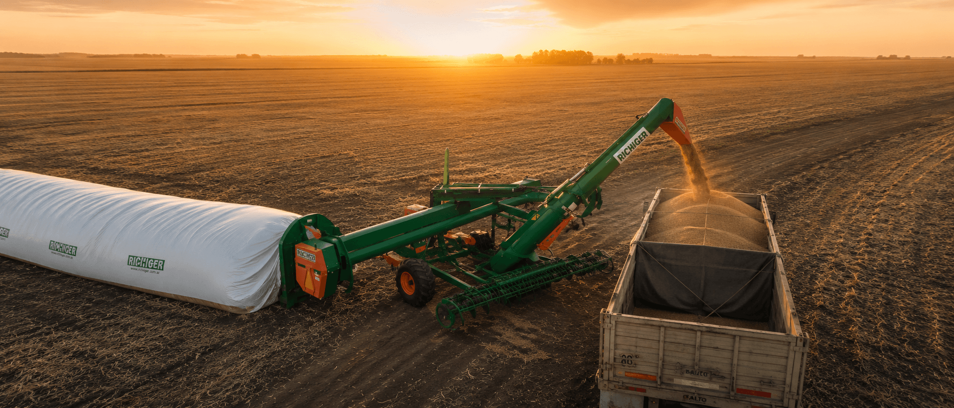 Extractora de granos cargando un camión al atardecer en un campo argentino, junto a un silobolsa